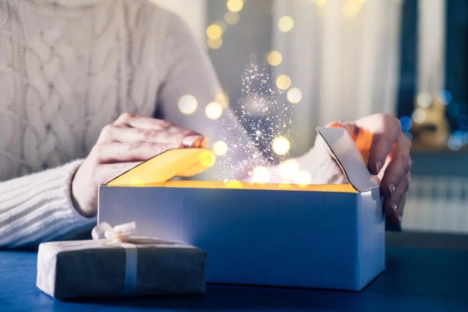 a woman is opening a gift box with a light shining out of it